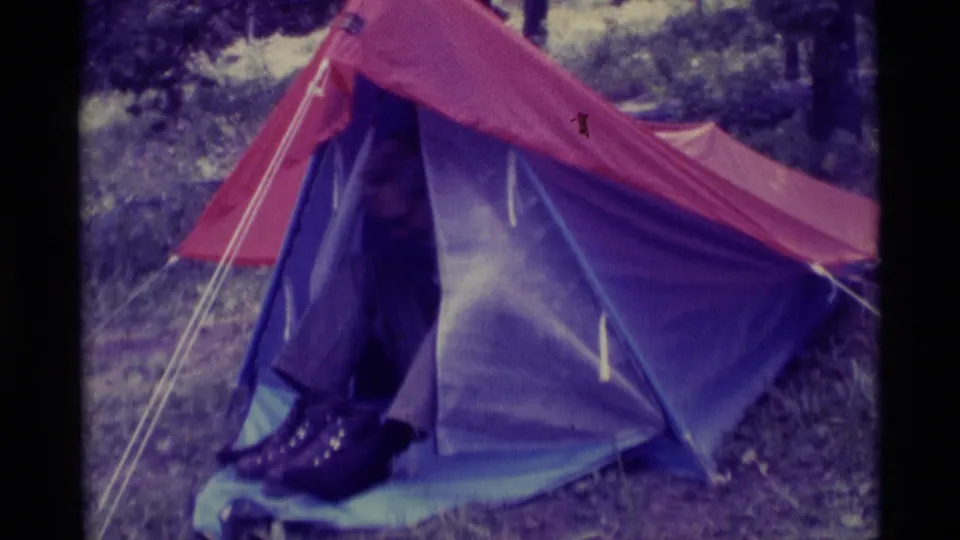 An adult camper in the Agate Springs, Montana home movie sits at the entrance of the red and purple tent.