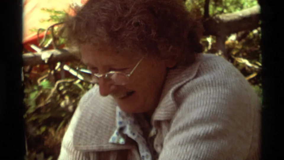 A closer 1975 Montana view shows the woman in glasses leaning down while preparing food at the campsite.