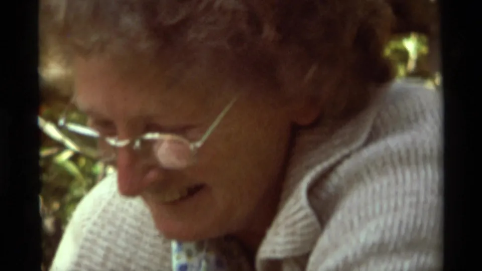 Soft 8mm close-up from the 1975 Montana campsite shows the woman with glasses looking down while working by hand.