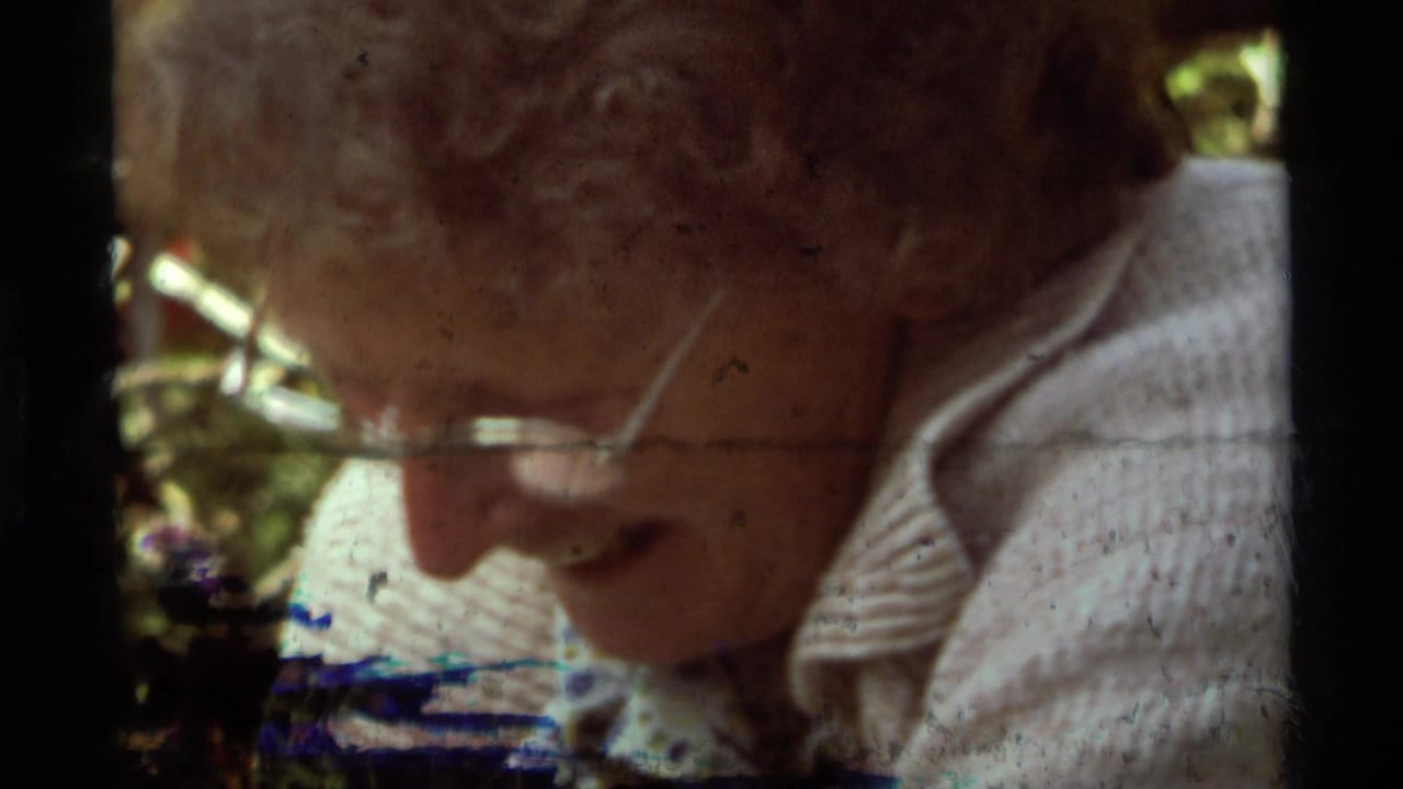Close view of an older person's face beside dark film edges and campsite color in the background.