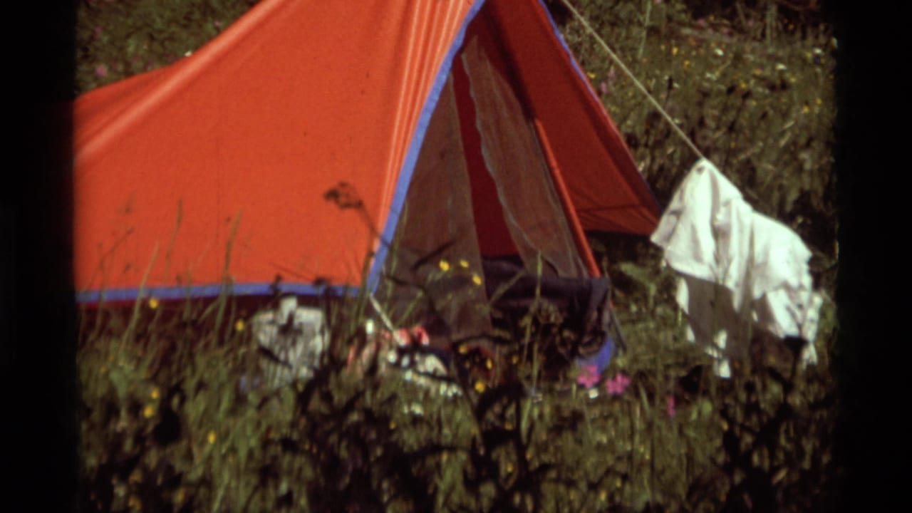 Red campsite tent at Agate Springs, Montana, in 1975, with tall grass, guy lines, hanging clothing, and scattered gear visible.