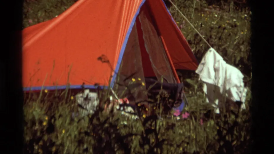 Red campsite tent at Agate Springs, Montana, in 1975, with tall grass, guy lines, hanging clothing, and scattered gear visible.