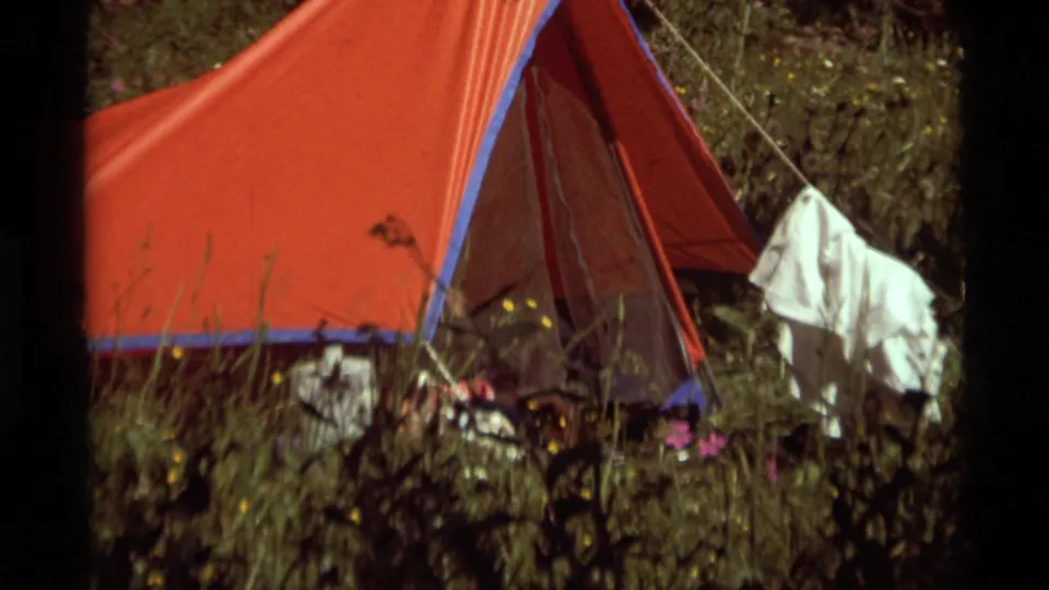 1975 8mm view of the Agate Springs campsite, showing a red tent, surrounding grass, taut lines, and clothing hanging near the entrance.