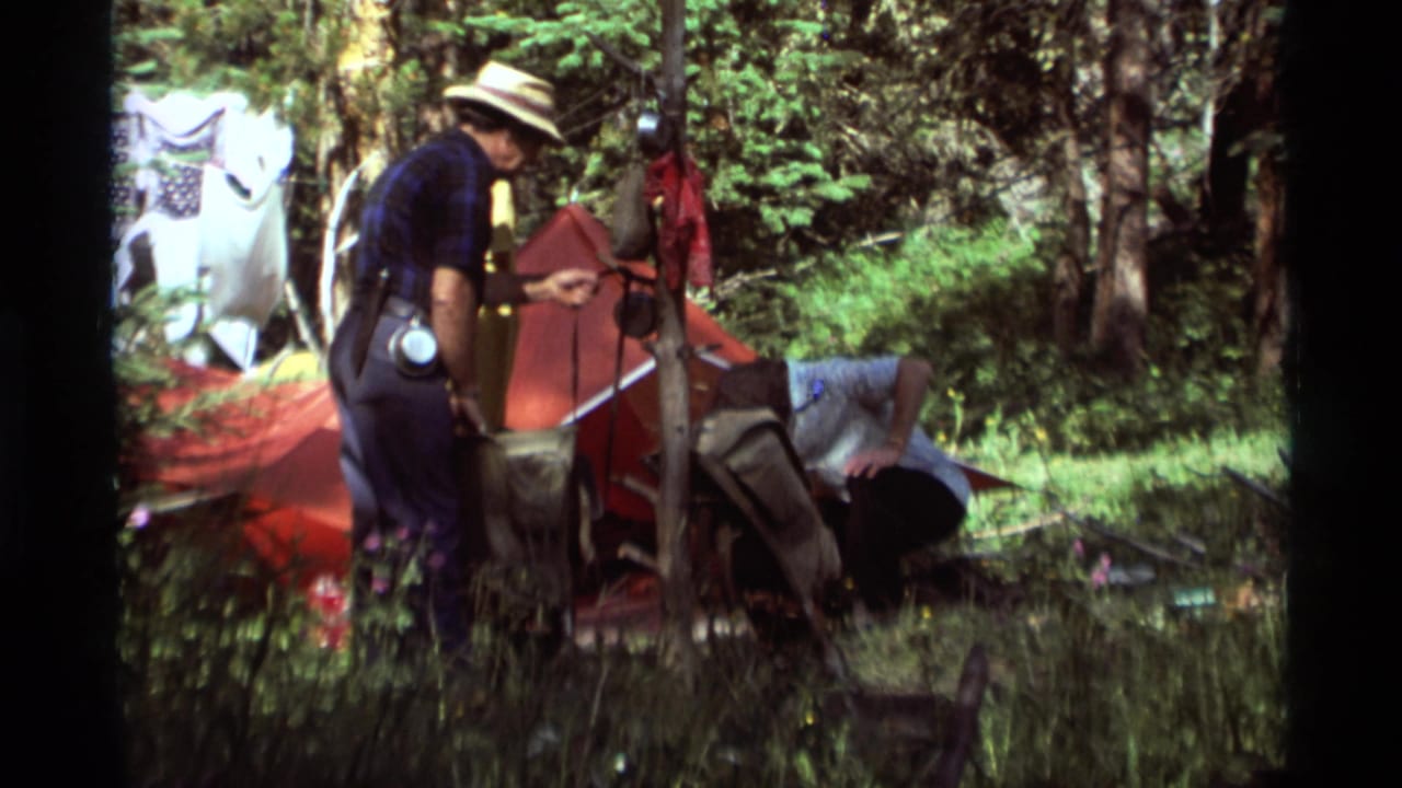 1975 Agate Springs, Montana 8mm frame showing adults working around a red tent in a wooded campsite.