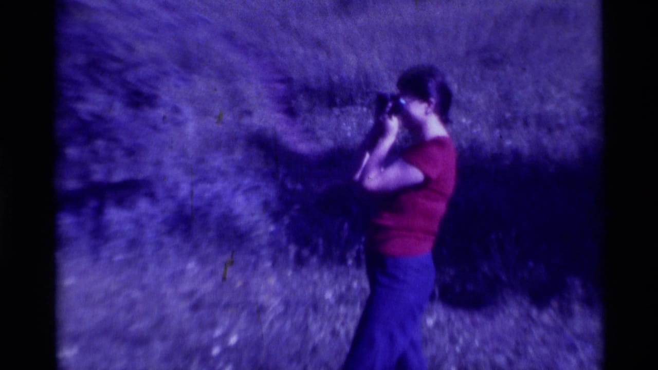 In 1975 Agate Springs, Montana home-movie footage, a woman in a red shirt and blue pants looks through a scope outdoors.