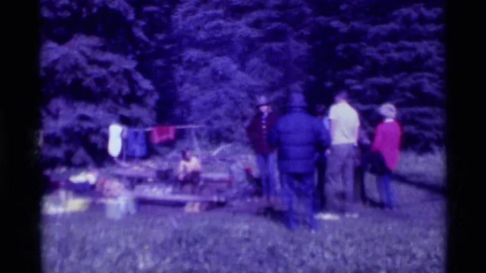 A group stands near outdoor camp gear, hanging clothes, and a grassy area in the Agate Springs home-movie scene.