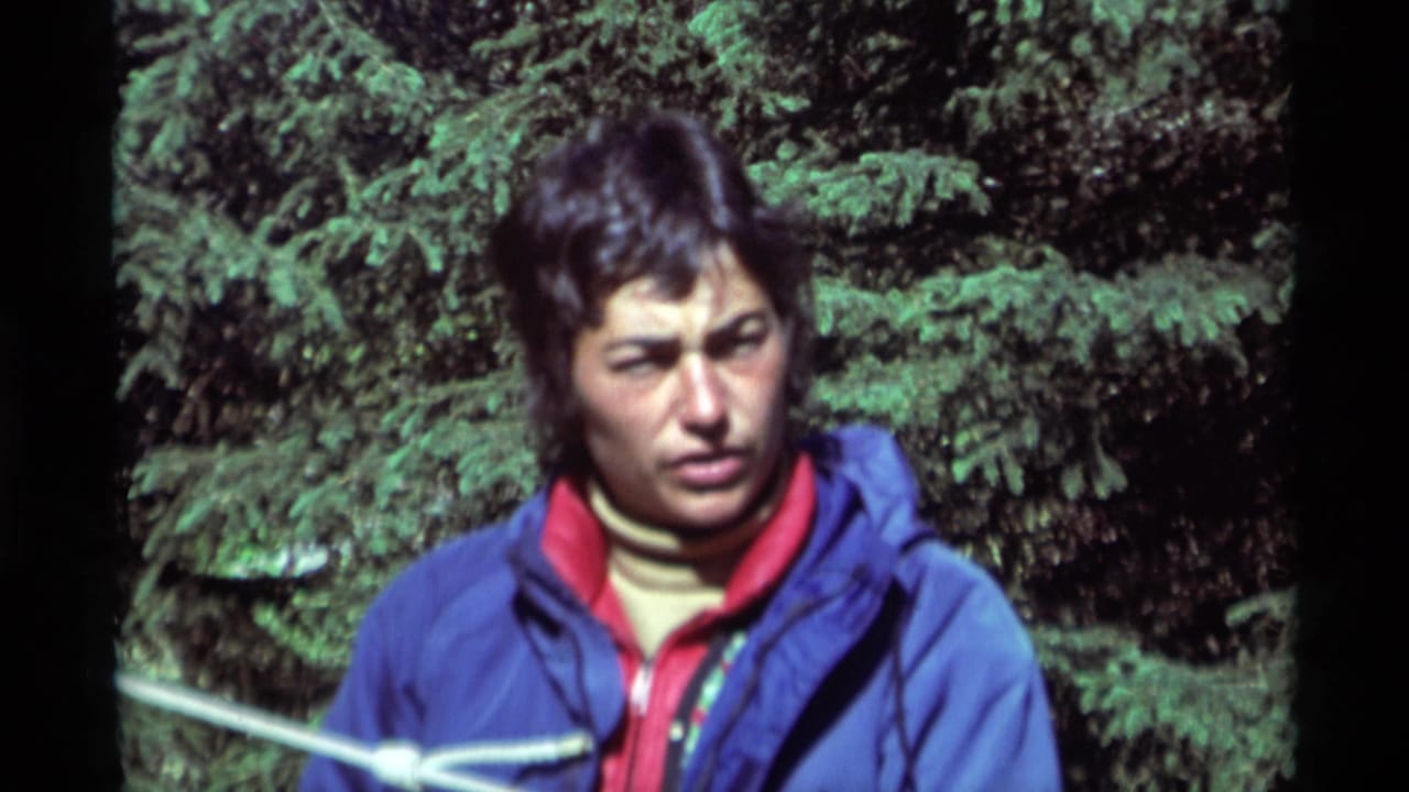 In 1975 Agate Springs, Montana footage, a young man in a blue jacket and red collar stands near a white rope against dense evergreens.