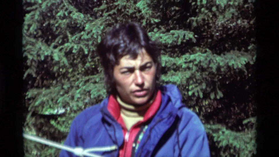 In 1975 Agate Springs, Montana footage, a young man in a blue jacket and red collar stands near a white rope against dense evergreens.