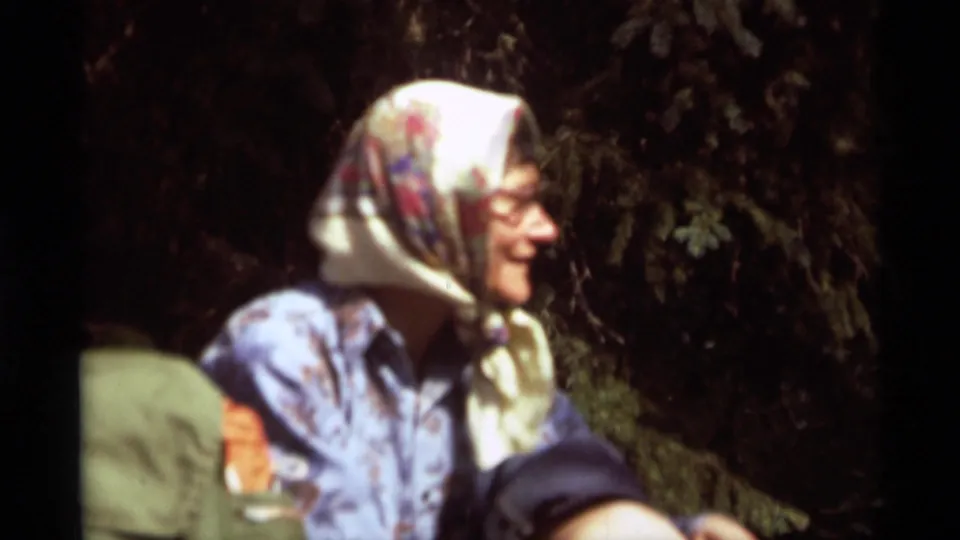 1975 Agate Springs frame showing a woman in a patterned headscarf seated among adults under evergreen branches.