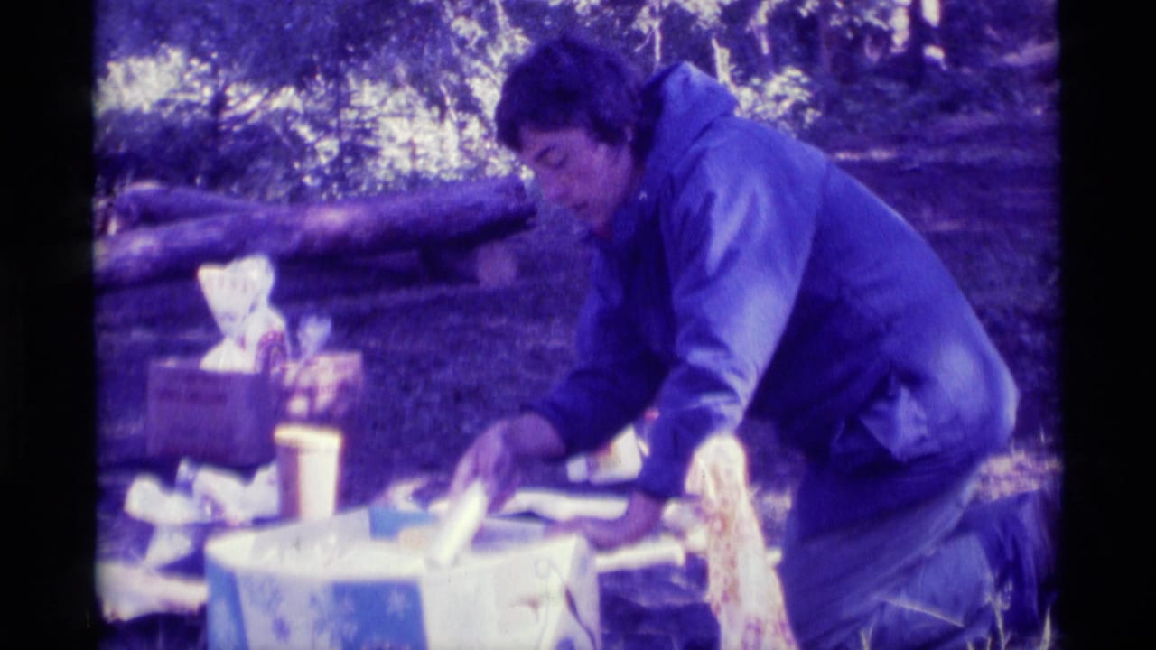 1975 8mm home-movie frame from Agate Springs, Montana, showing a person in a blue jacket arranging picnic food outdoors.