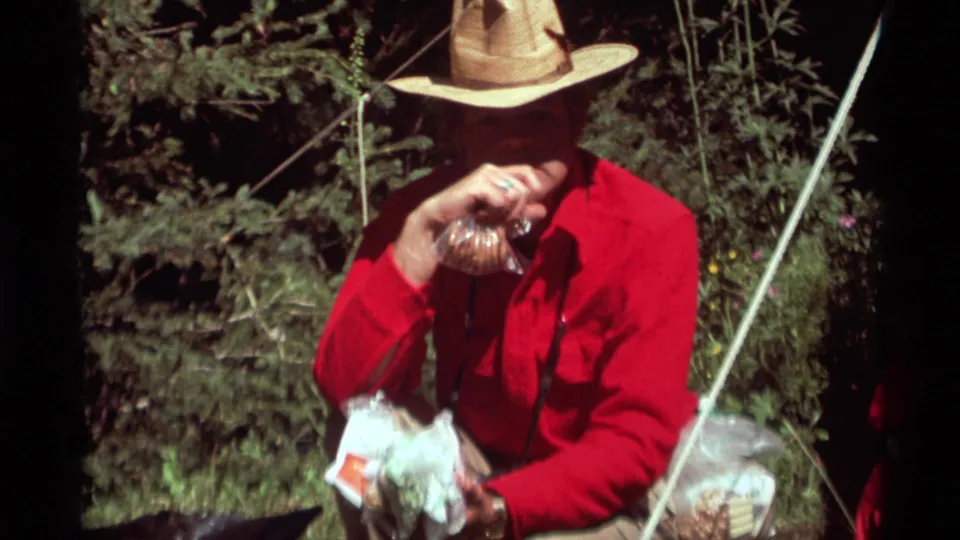 In the wooded Agate Springs scene, the man brings a wrapped food item to his mouth while seated near bags and a visible tent line or cord.
