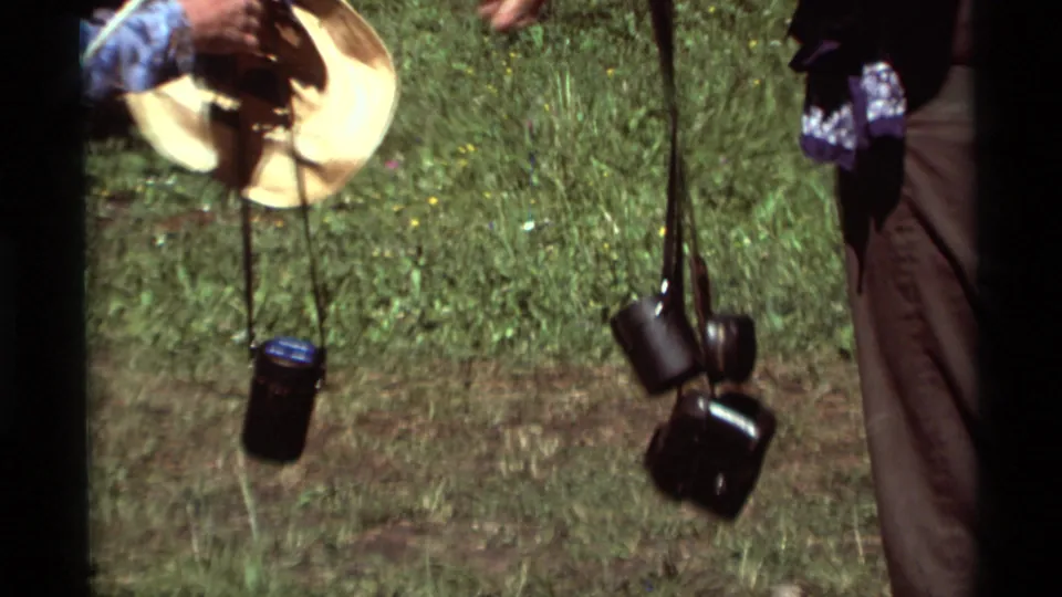 1975 8mm Montana home-movie frame showing a close view of hikers' hanging gear near grass and trees.