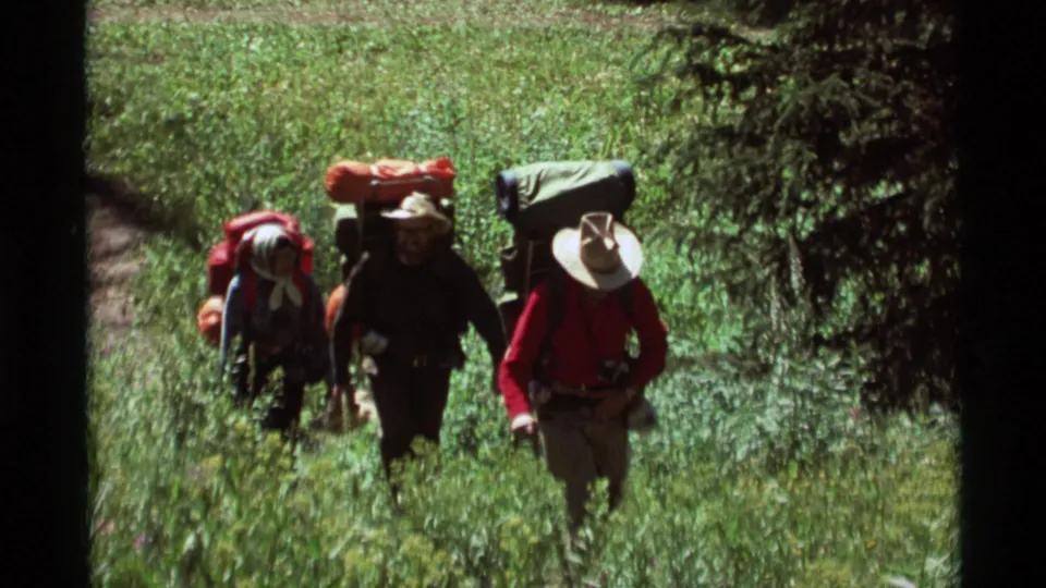 1975 8mm frame of three backpackers on a wooded trail in Agate Springs, Montana, with hats and frame packs visible.