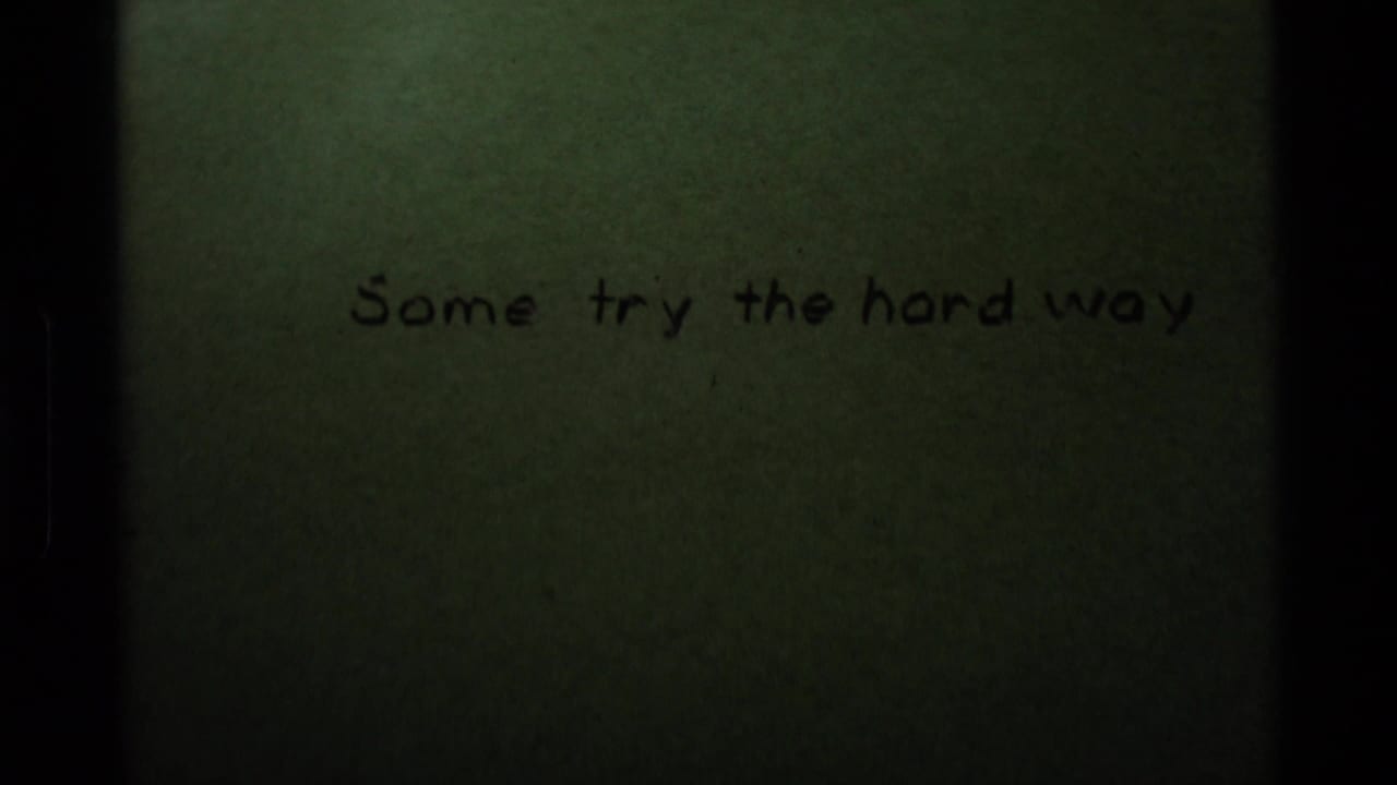 1975 8mm sample frame showing a greenish handwritten title card reading “Some try the hard way,” with dark film borders.