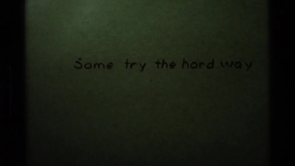 1975 8mm sample frame showing a greenish handwritten title card reading “Some try the hard way,” with dark film borders.