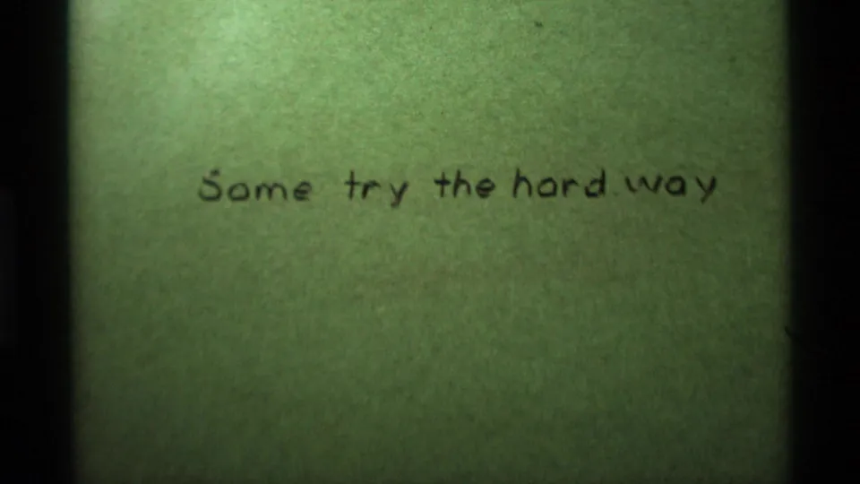 8mm title-card frame with handwritten wording on a pale green surface and visible archival grain.