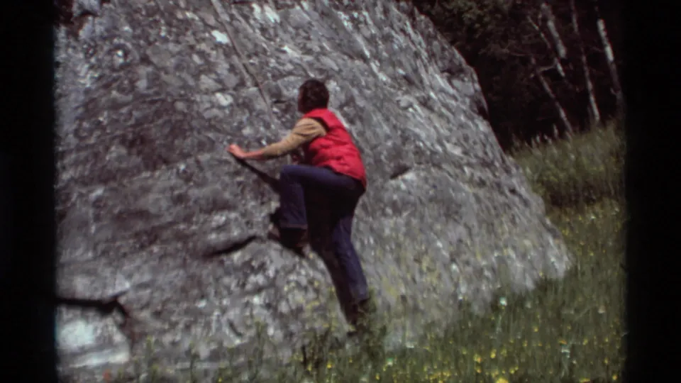 A red-vested climber raises a foot onto the gray rock formation at Agate Springs, Montana, in 1975 home-movie footage.