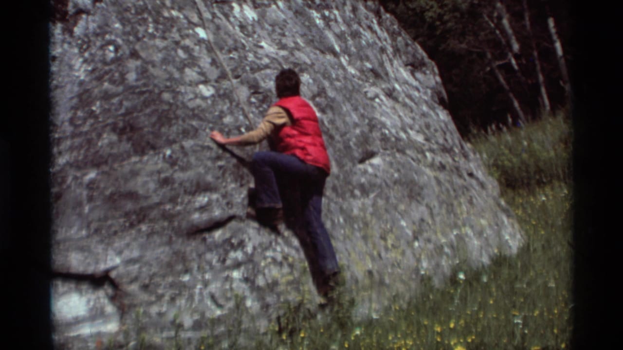At Agate Springs, Montana in 1975, a young climber in a red vest begins moving across a large gray boulder.