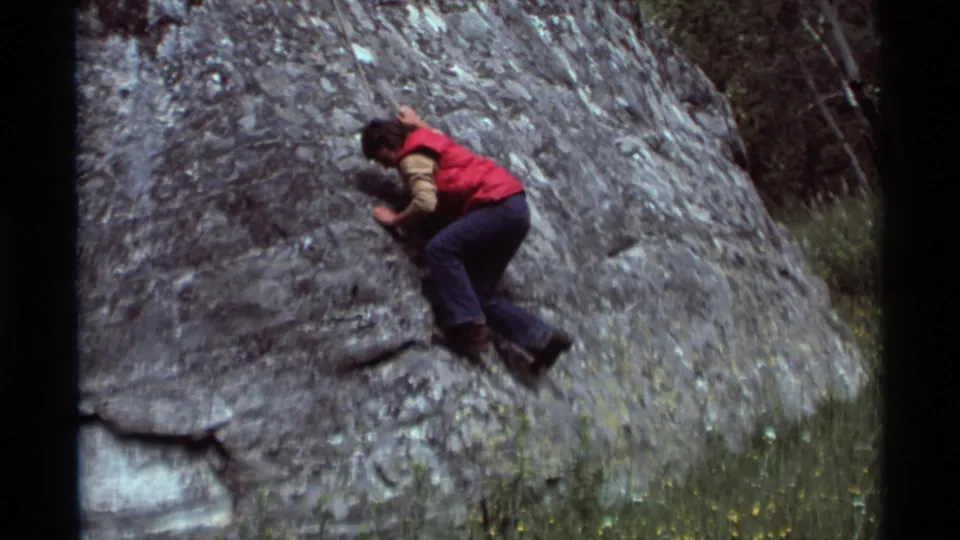 The climber presses close to the gray boulder during a careful traverse in the 1975 Montana home-movie footage.