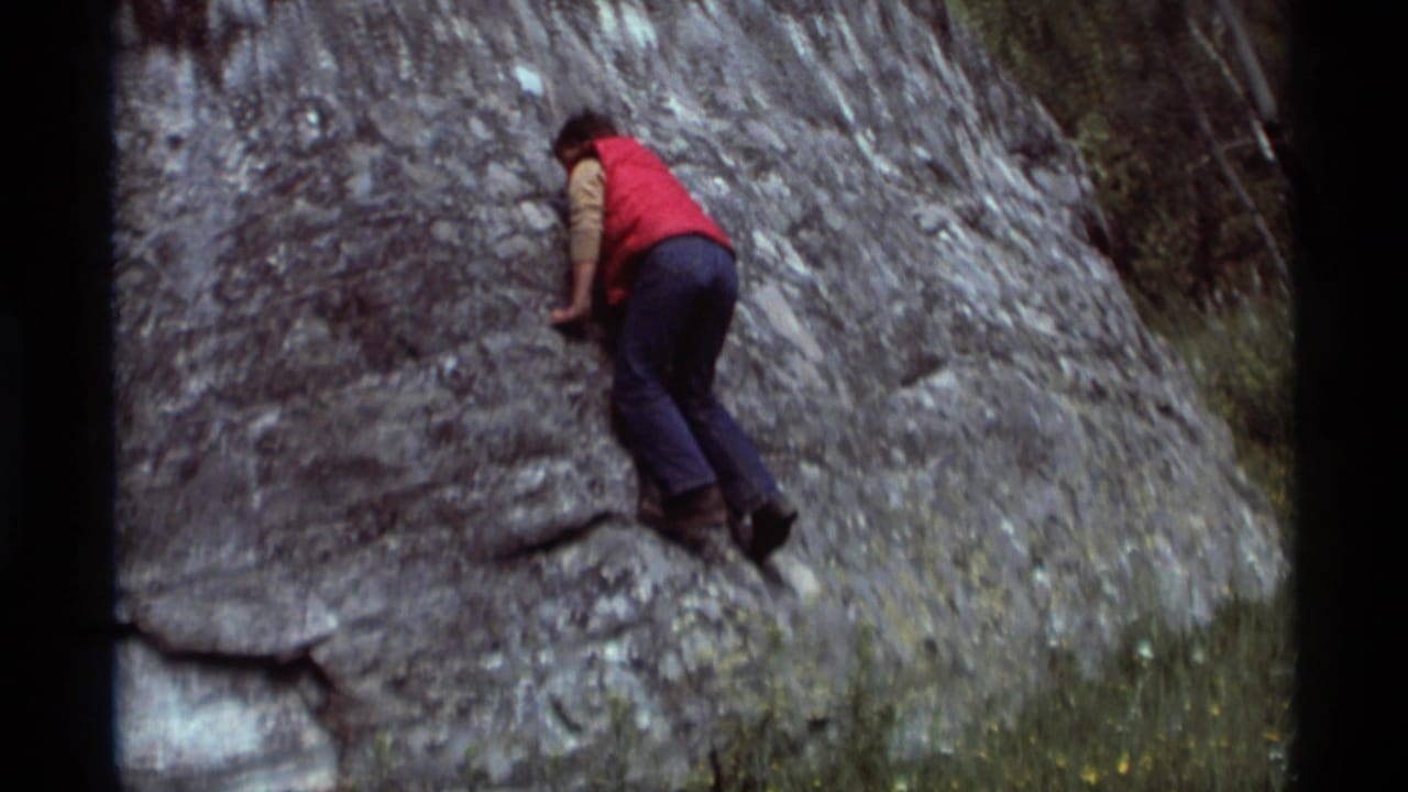 1975 Agate Springs, Montana 8mm frame showing a young man in a red vest carefully climbing a gray rock face.