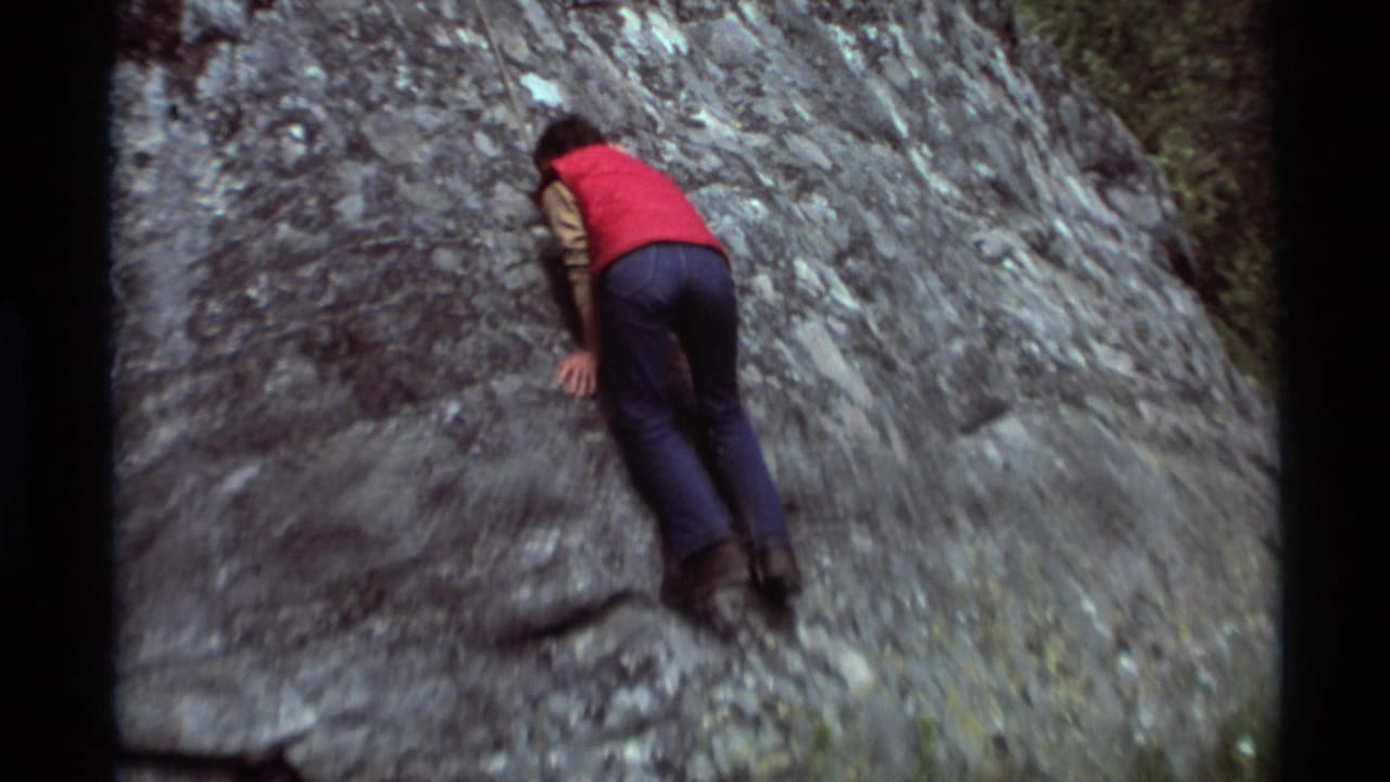 Rear view of the climber on the steep rock face, framed by 8mm film borders in the 1975 Montana home movie.