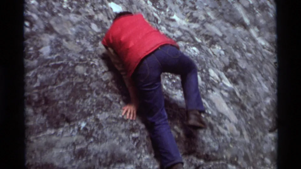 Close 8mm frame of the red-vested climber leaning into the textured rock at Agate Springs, Montana, in 1975.