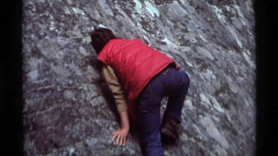 In 1975 Agate Springs, Montana footage, a person in a red vest and blue jeans leans into a steep gray rock face while climbing.