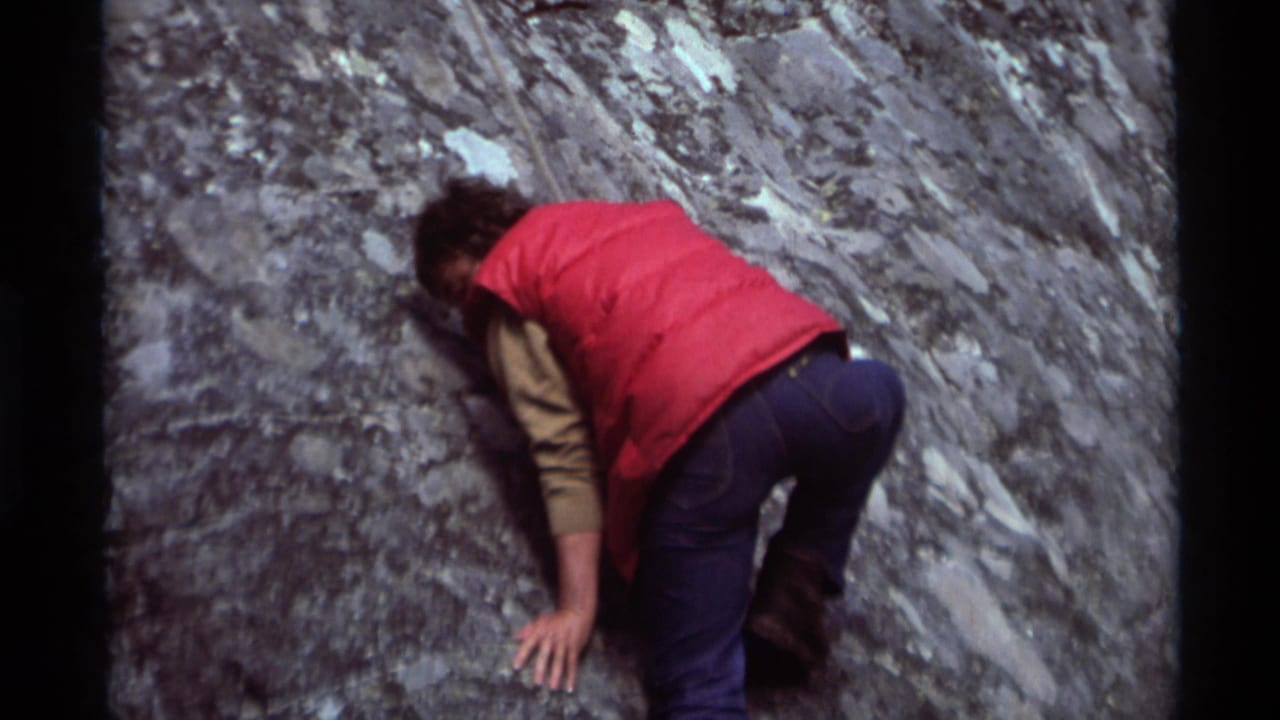 Person crouched against a gray rock face while climbing.
