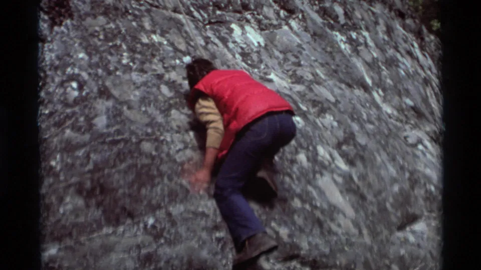 A person in a red vest and blue jeans continues climbing across the steep Agate Springs rock face in 1975 home-movie footage.