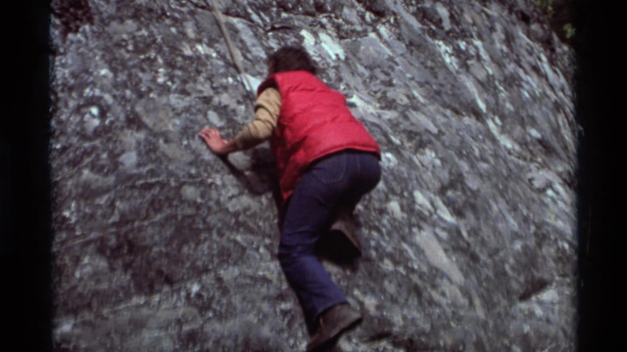 1975 Agate Springs, Montana home-movie frame showing a climber in a red vest and jeans working up a rugged gray rock face.