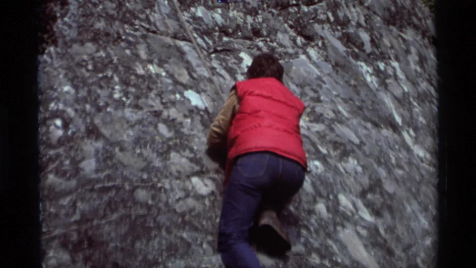 1975 Agate Springs, Montana 8mm frame showing a climber from behind, balancing on a rough rock surface in jeans and boots.