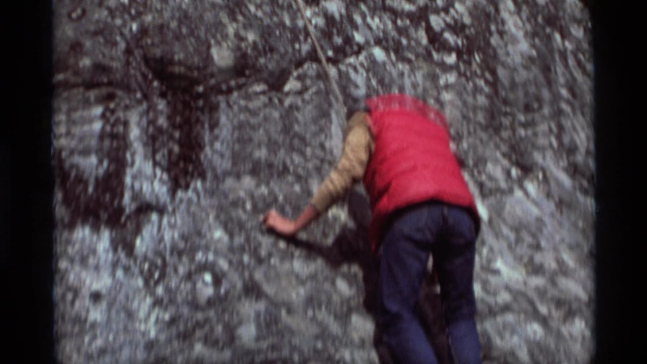 1975 Agate Springs, Montana home-movie frame showing a climber in a red vest pressed against a gray rock face.