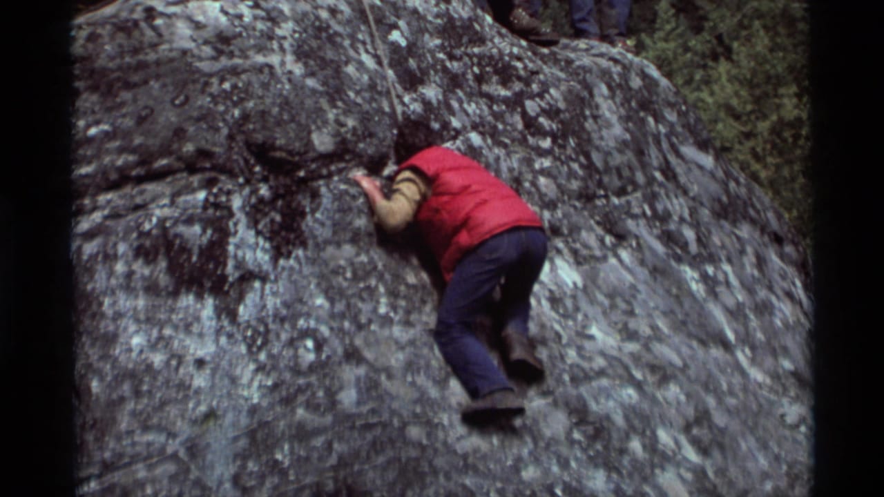 At Agate Springs, Montana in 1975, a climber in a red vest and jeans moves up a steep rock face on 8mm home-movie footage.