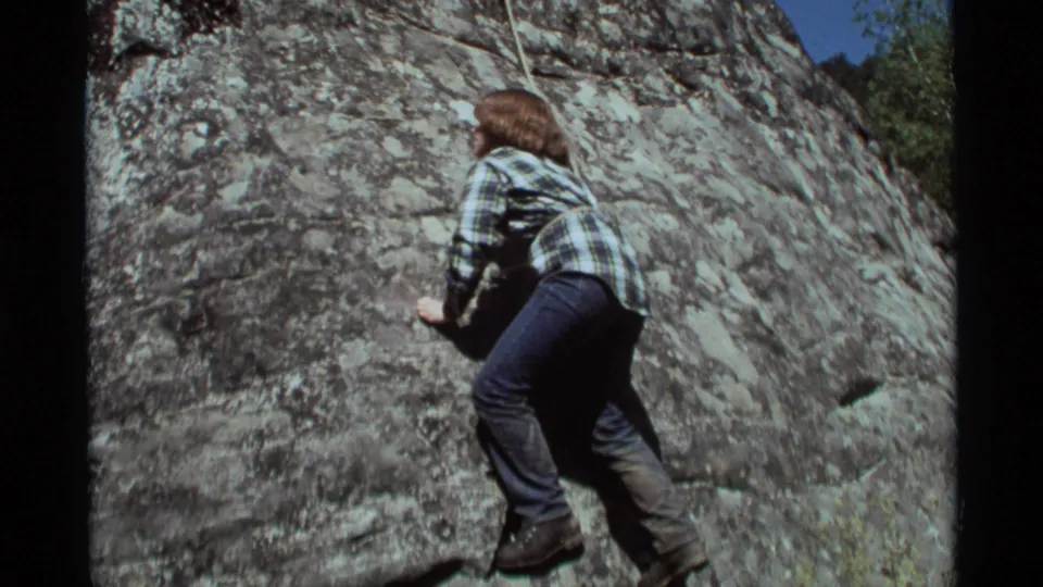 1975 Agate Springs, Montana frame of a young climber seen mostly from behind while scaling a rough rock face in daylight.