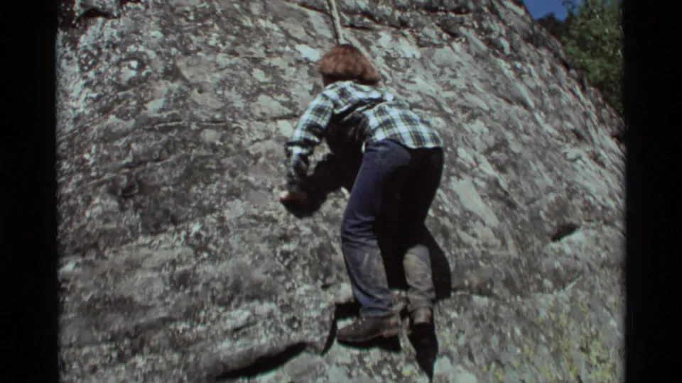 1975 Agate Springs, Montana frame of the young climber continuing upward on the textured rock face, filmed in a close home-movie view.