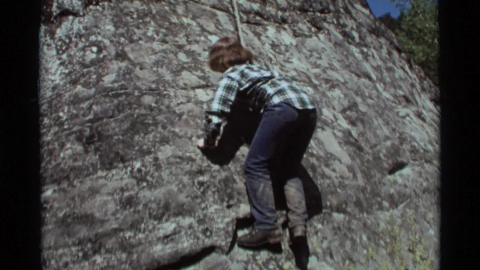 In 1975 Agate Springs, Montana footage, a young person in casual clothes climbs a lichen-covered rock face using a rope.