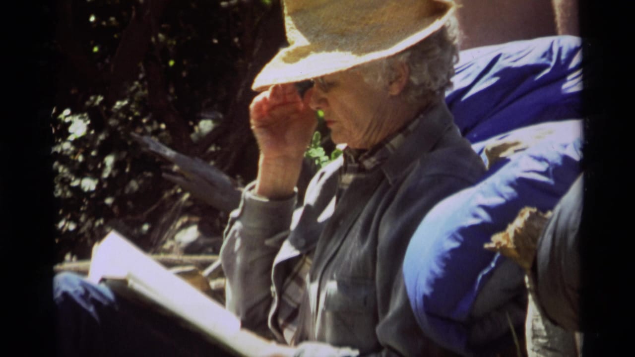 Older man in a straw hat and gray jacket reads outside in Agate Springs, Montana, in 1975 home-movie footage.