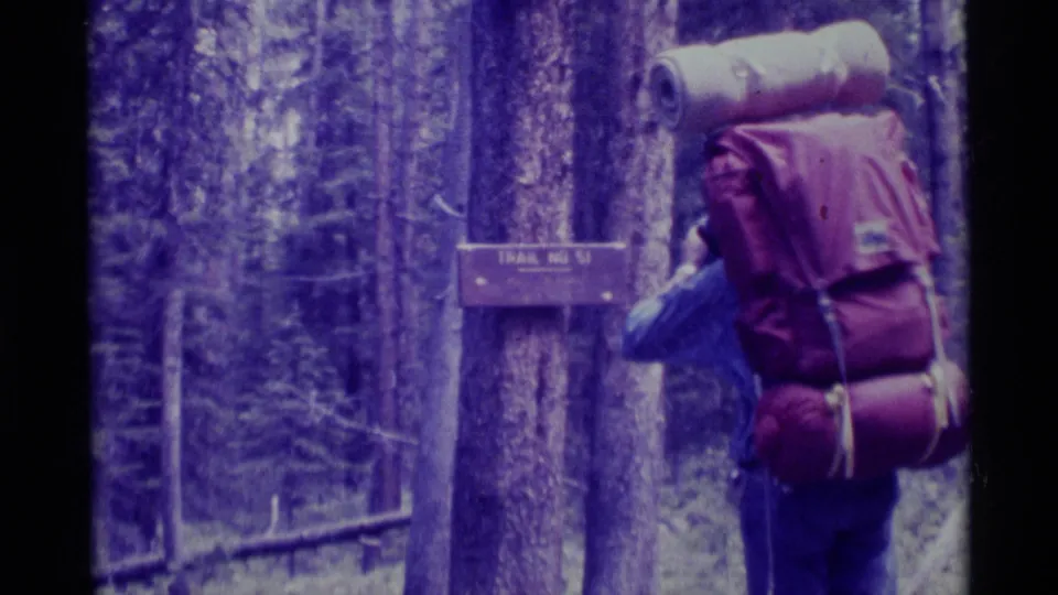 1975 Montana 8mm frame showing a hiker with a large backpack near a wooden Trail No. 51 sign among trees.