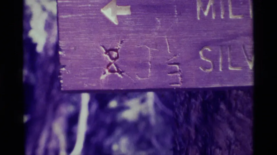 Extreme close-up of the weathered wooden trail sign, showing an arrow, carved marks, and partial Silver Pass lettering.