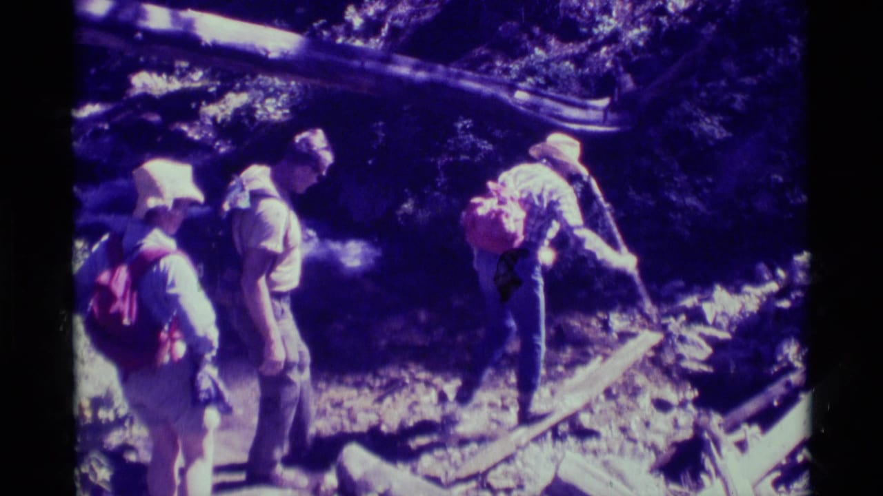 Three adult hikers in hats and backpacks pause on uneven forest ground in Agate Springs, Montana, in 1975 home-movie footage.