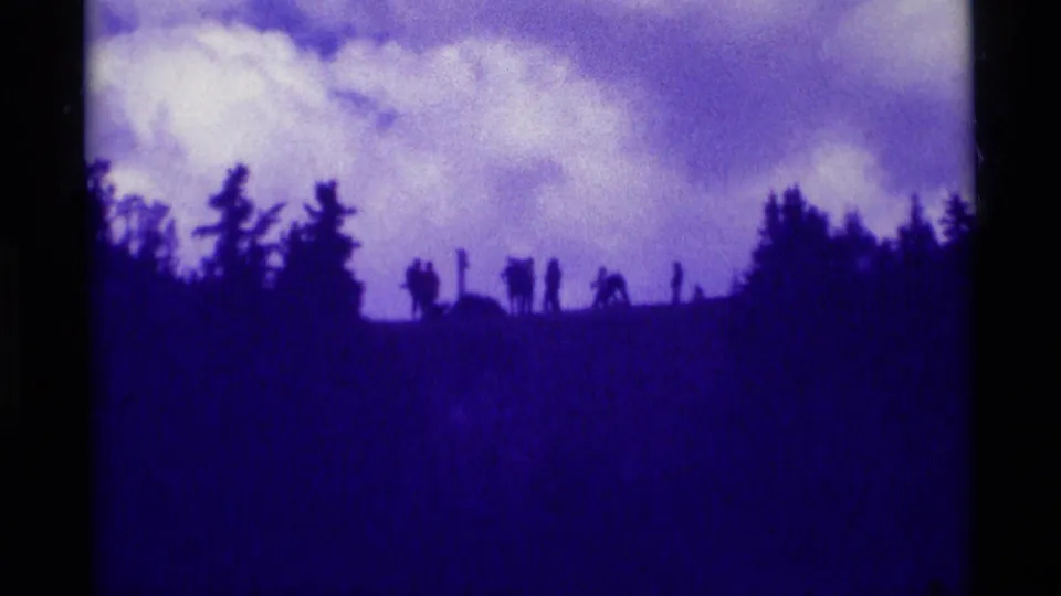 1975 Agate Springs frame with distant figures silhouetted on a hillside, framed by trees and a bright cloudy sky.