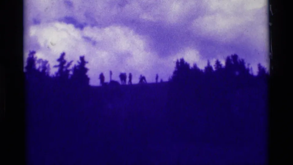 1975 8mm Agate Springs, Montana view of a dark tree-lined ridge silhouetted below large pale clouds.
