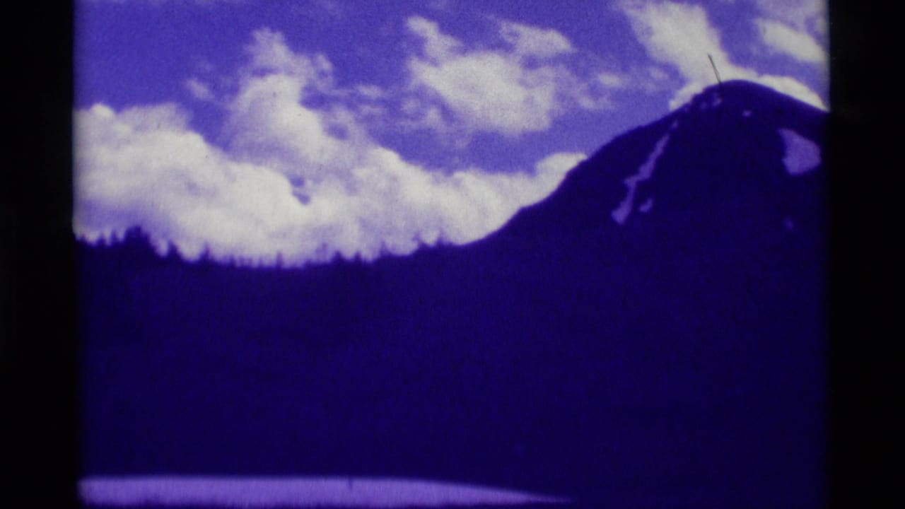 1975 Agate Springs, Montana 8mm frame showing a dark mountain ridge, clouded sky, and forested slope with a strong purple film cast.