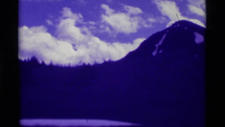 1975 Agate Springs, Montana 8mm frame showing a dark mountain ridge, clouded sky, and forested slope with a strong purple film cast.