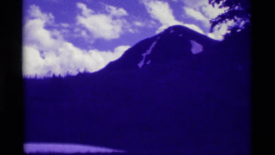 Agate Springs, Montana mountain view with a dark ridge, scattered clouds, and tree silhouettes in purple-shifted 8mm footage.