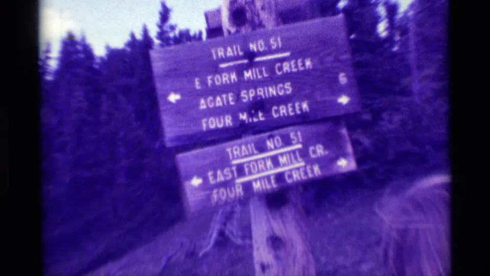 Close 1975 Agate Springs trail-sign frame showing directions to East Fork Mill Creek and Four Mile Creek in purple-tinted 8mm film.