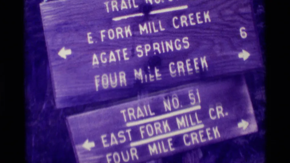 1975 8mm frame from Agate Springs, Montana, showing weathered wooden Trail No. 51 direction signs with arrows and creek names.
