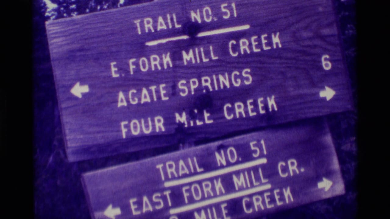 Vintage 8mm frame shows Trail No. 51 signage for East Fork Mill Creek, Agate Springs, and Four Mile Creek in a wooded setting.