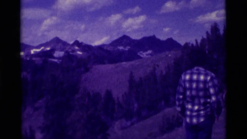 Agate Springs, Montana 8mm frame shows a plaid-shirted adult looking toward snow-streaked mountains and forested slopes under clouds.