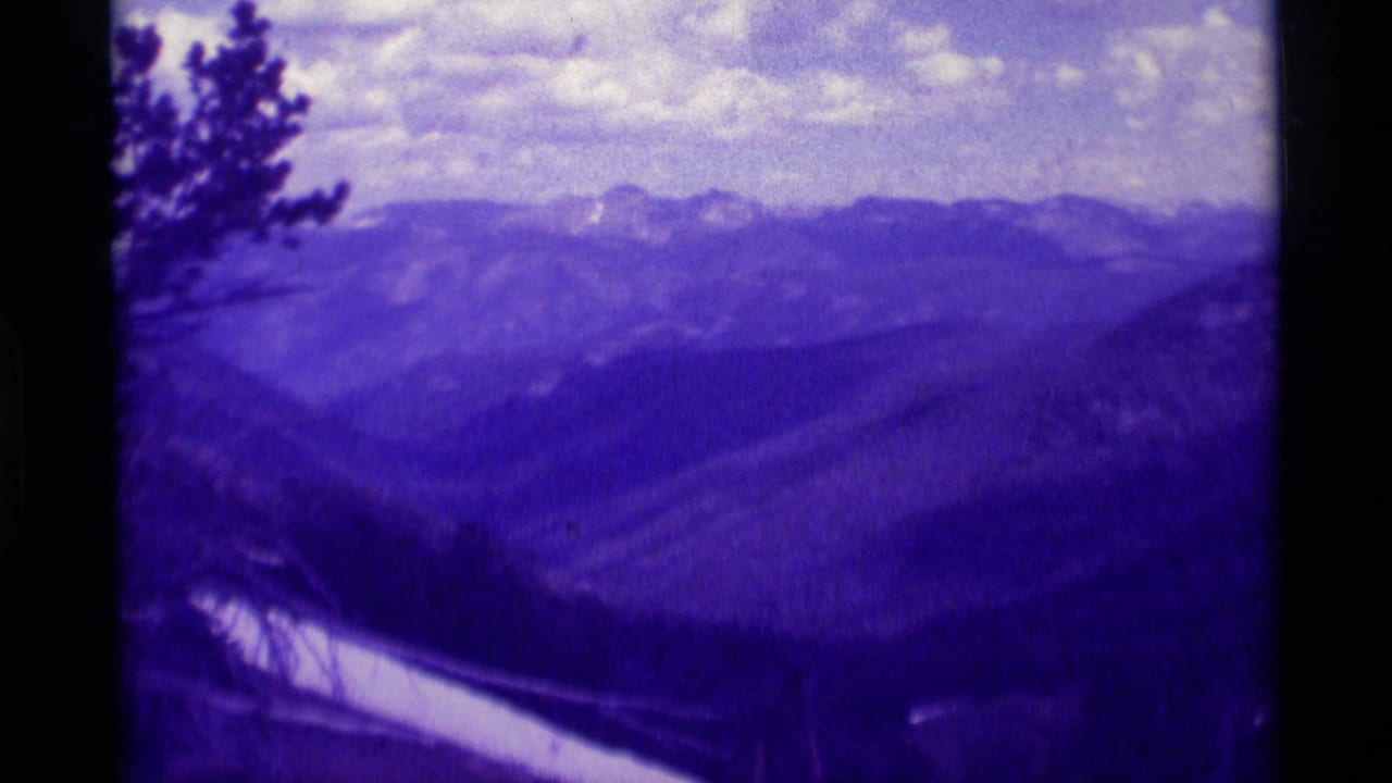 1975 8mm view near Agate Springs, Montana, showing layered mountain ridges, pale snow patches, and an evergreen at the left edge.